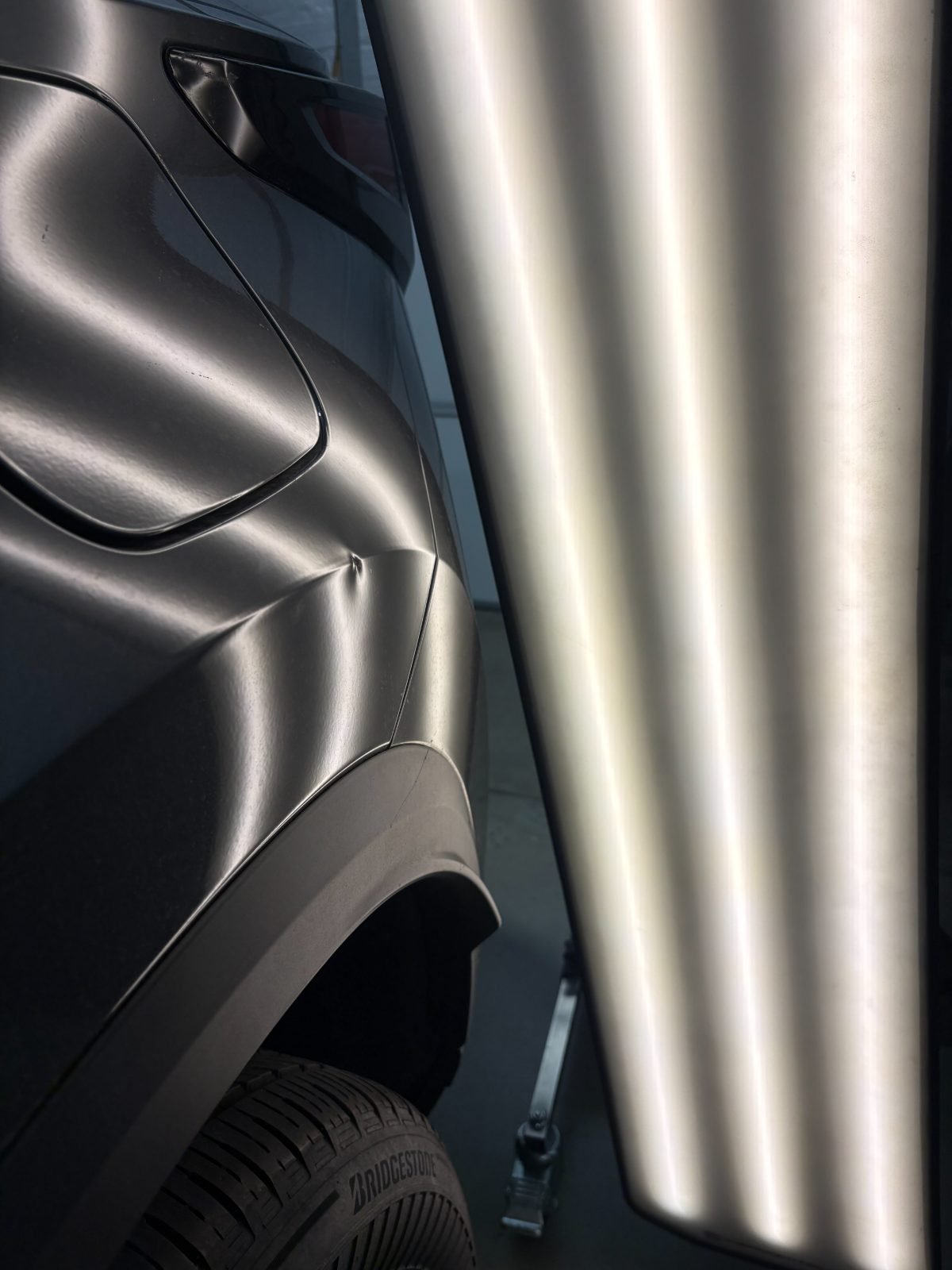 PDR light board reflected across a dark quarter panel, its straight bands bending where hail dents sit