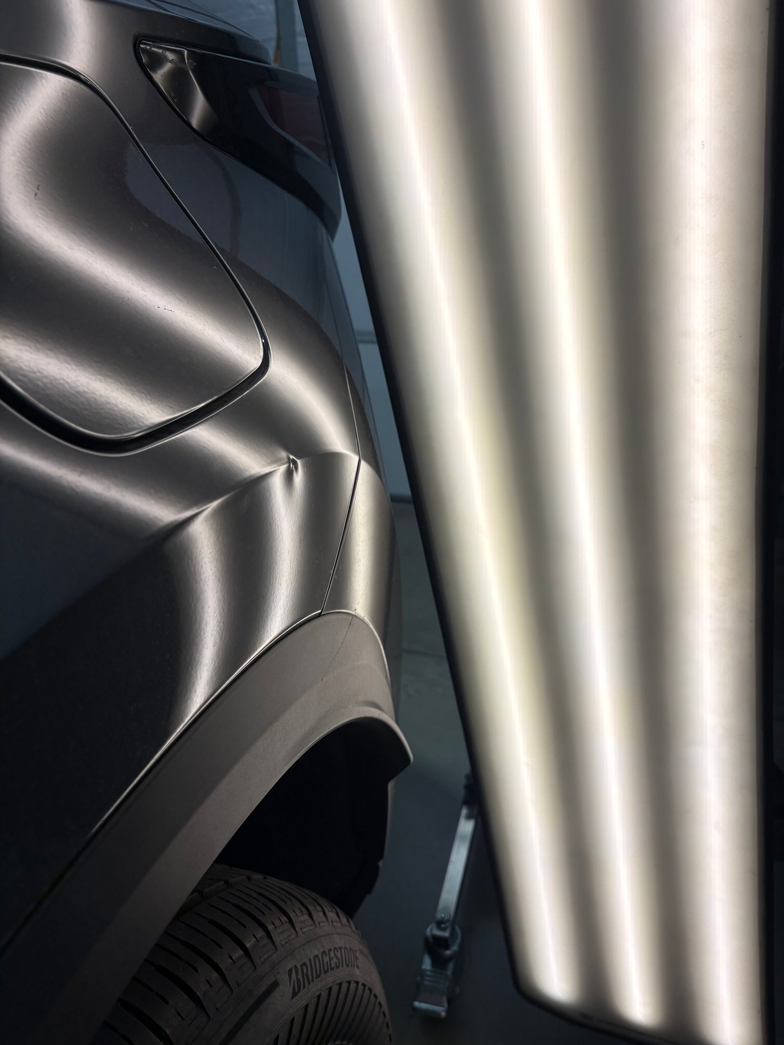 PDR light board reflected across a dark quarter panel, its straight bands bending where hail dents sit