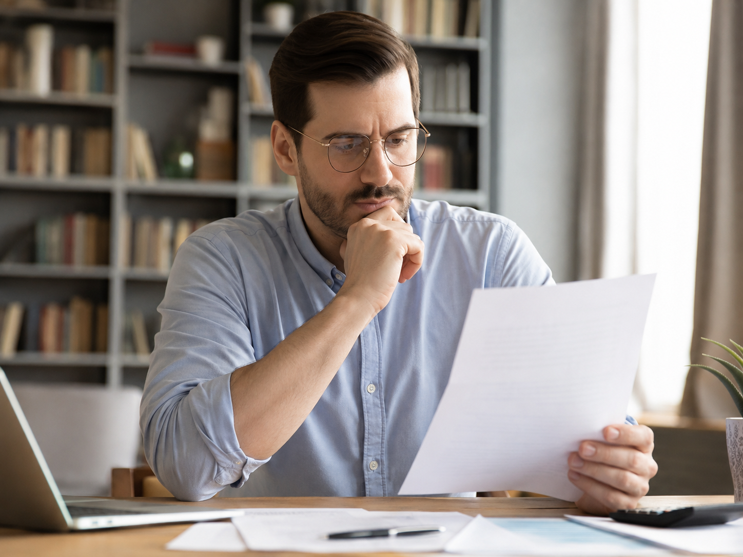A policyholder at a desk reading a carrier's written claim decision, calculator and paperwork in front of him